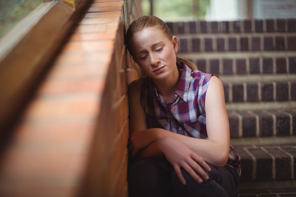 Menina chateada, encostada na parede, representando uma Adolescente com epilepsia.