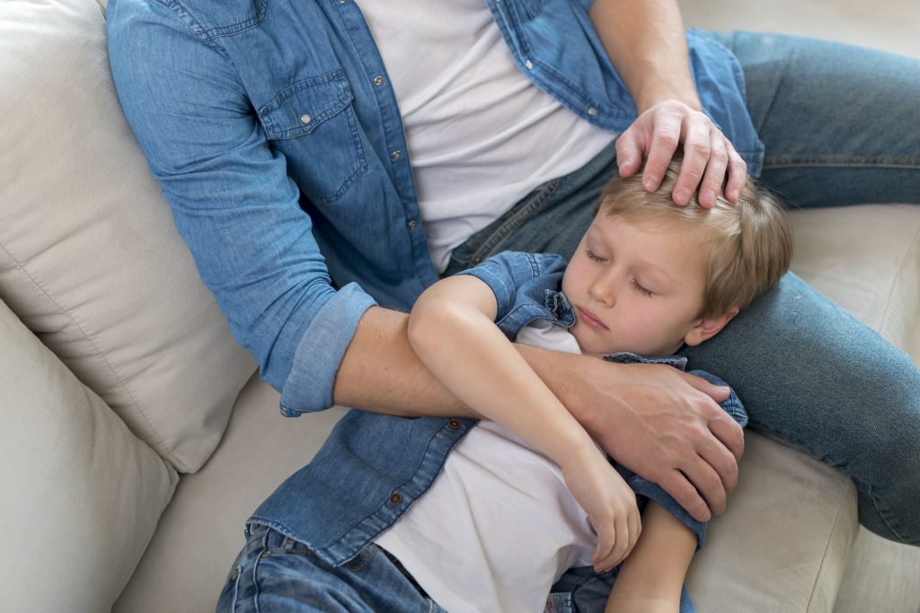 Pai acalentando filho no sofá, preocupado com os efeitos colaterais dos anticonvulsivantes